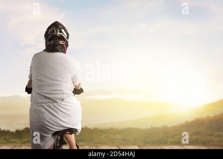 Vue arrière d'une femme asiatique avec un casque de vélo vélo sur un chemin en bois avec fond de lumière du soleil Banque D'Images