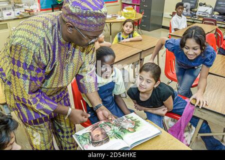 Miami Florida,Overtown,Frederick Douglass Elementary School,professeur homme tenue habillée, littéraire costume lecture livre caractère fictif, hispanique Banque D'Images