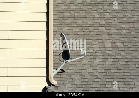 Antenne à disque satellite sur le côté du bâtiment avec bardeaux de toit et vidange de la gouttière Banque D'Images