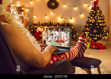 Père Noël en costume avec barbe blanche discutant avec des petits-enfants en ligne sur ordinateur portable pendant la vidéo Banque D'Images