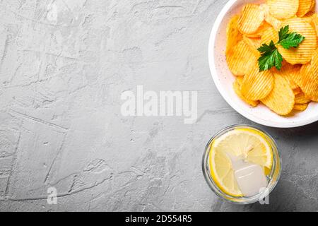 Glace fraîche eau froide buvez avec du citron près de chips de pomme de terre dorée avec feuille de persil dans un bol en bois sur fond de béton, vue du dessus de l'espace copie Banque D'Images