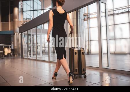 Femme portant une robe noire et portant une valise Banque D'Images