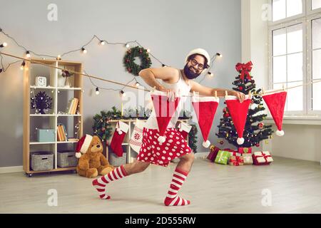 Drôle, fou, homme dans un débardeur, chaussettes, short et dans un chapeau Santa pend ses chapeaux sur une corde. Banque D'Images