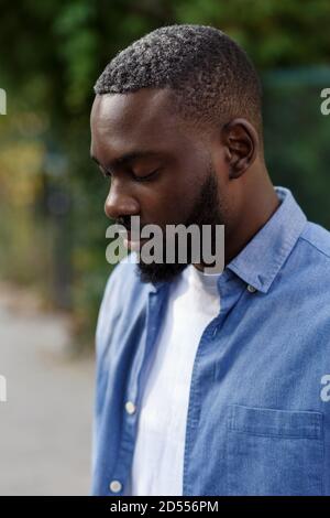 Gros plan sur un homme afro-américain sérieux aux yeux fermés. Beau jeune homme calme dans une chemise en denim bleu dans la rue Banque D'Images