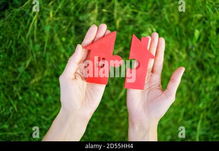 Maison rouge avec une forme de deux parties de puzzle dans les mains humaines Banque D'Images