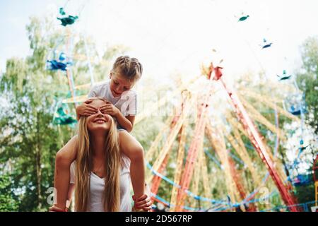 La fille est assise sur les épaules. Petite fille joyeuse sa mère a un bon moment dans le parc ensemble près des attractions Banque D'Images