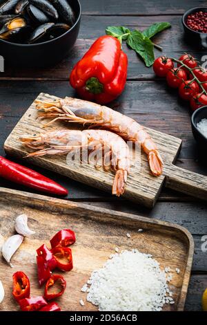 Paella traditionnelle valenciana ingrédients crus avec crevettes, moules, riz et calmar sur fond de bois rustique foncé Banque D'Images