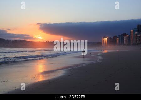 Un homme marche le long de la plage de San Lorenzo au lever du soleil dans la ville de Gijon. Mer de Cantabrie. Asturies. Espagne Banque D'Images