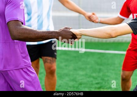groupe multiethnique de jeunes jouant au football tenant les mains. les noirs et les blancs tenant les mains jouant au sport, symbole du pouvoir unificateur de la soc Banque D'Images