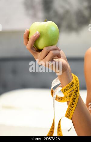 Femme tenant une pomme verte fraîche et saine dans sa main avec un ruban à mesurer enroulé autour de son bras dans un concept de régime et de perte de poids en gros plan Banque D'Images