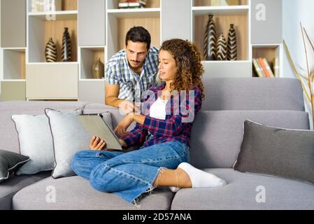 Un jeune couple regarde ensemble les médias sur une tablette détendez-vous dans le salon à la maison dans un cadre personnel concept de divertissement Banque D'Images