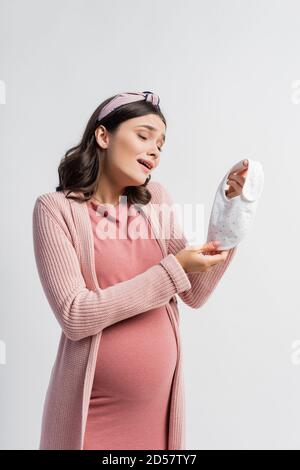 femme enceinte regardant un petit bavoir de bébé isolé sur blanc Banque D'Images