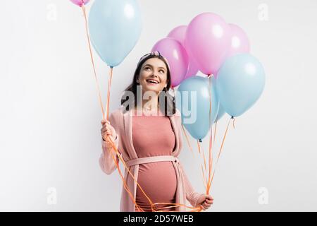 femme joyeuse et enceinte en robe tenant des ballons et regardant up isolé sur blanc Banque D'Images