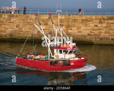 Un bateau de pêche rouge retourne au port de Whitby sur la côte est du North Yorkshire, Angleterre, Royaume-Uni - pris en fin d'après-midi Banque D'Images