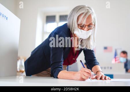 Portrait d'une femme votant avec masque facial dans le lieu de vote, élections et concept du coronavirus. Banque D'Images