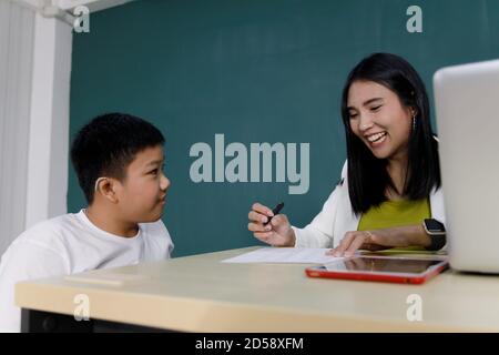 Un jeune garçon asiatique qui a des problèmes d'audition fait ses devoirs avec son professeur en classe. Banque D'Images