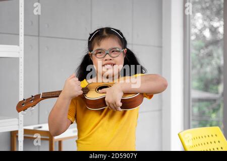 Bonne fille asiatique avec le syndrome de Down jouer ukulele. Concept d'apprentissage des enfants handicapés. Banque D'Images