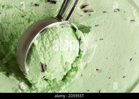 Gros plan de la glace à la menthe au chocolat en train d'être rasée par une pelle mécanique à servir. Banque D'Images