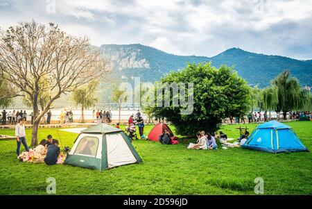 Kunming Chine , 3 octobre 2020 : Chinois appréciant des vacances dans le parc de Dianchi Haigeng avec des tentes sur l'herbe et le lac et les collines de l'ouest dans backgr Banque D'Images