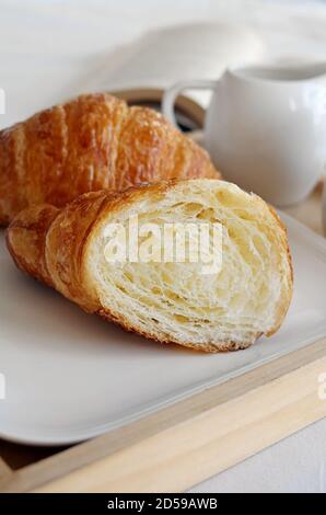 Gros plan d'un croissant en deux sur un plateau de petit déjeuner avec un livre et une verseuse Banque D'Images