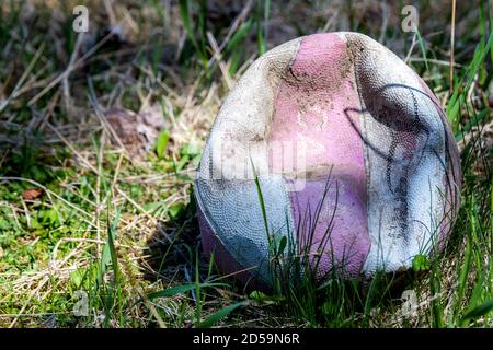 Un vieux basket-ball, délavé et dégonflé, allongé dans l'herbe. Une partie de l'ombre et une partie de la lumière du soleil sur la balle. La balle est également sale. Banque D'Images