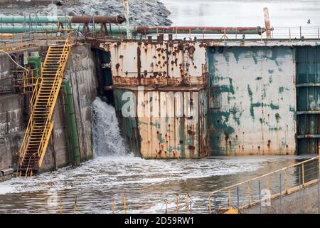 Un ancien quai sec qui n'est plus utilisé. Un torrent d'eau s'écoule dans le quai sec d'un coin. Escalier jaune descendant vers le bas. Banque D'Images