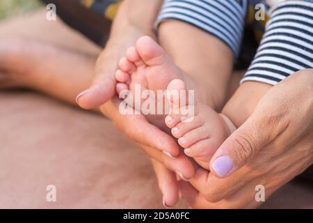 Les mains des mères maintiennent les jambes du bébé. Pieds nouveau-nés Banque D'Images