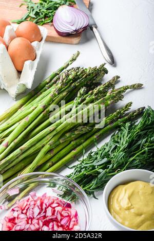 Œufs d'asperges et ingrédients de la vinaigrette française avec moutarde de dijon, oignon haché dans de l'estragon au vinaigre rouge sur fond blanc texturé, vue latérale. Banque D'Images