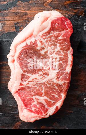 Steaks de bœuf cru sur des planches sombres en bois anciennes, vue du dessus. Banque D'Images