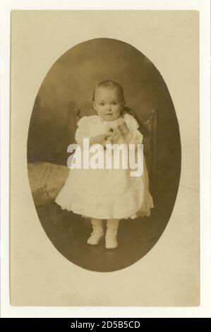 Début 1900 carte postale de bébé tout-petit, un an, tenant des fleurs artificielles prop R.-U. vers 1905 1906 Banque D'Images