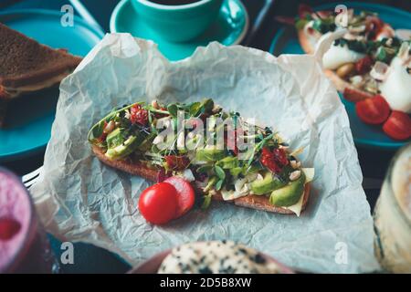 Pain grillé à l'avocat servi pour le déjeuner dans le café.délicieux sandwich avec tranché avocats, tomates séchées, micro verts servis sur papier parchemin pour le petit déjeuner Banque D'Images