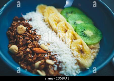 Repas végétarien pour le petit-déjeuner. Porridge aux flocons d'avoine, riz blanc bouilli, fruits en tranches, noix servies en bleu Bol en céramique pour le déjeuner dans le café vegan Banque D'Images