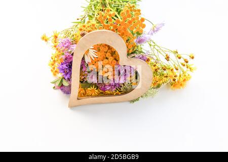 Bouquet de fleurs d'été sauvages en terre de tansy, de Marguerite blanche et de terrier épineux avec coeur décoratif en bois Banque D'Images