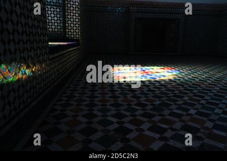 Cette chambre sombre est décorée de carreaux aux bordures colorées tandis que la lumière entre par une fenêtre illuminant le sol. Maroc Banque D'Images