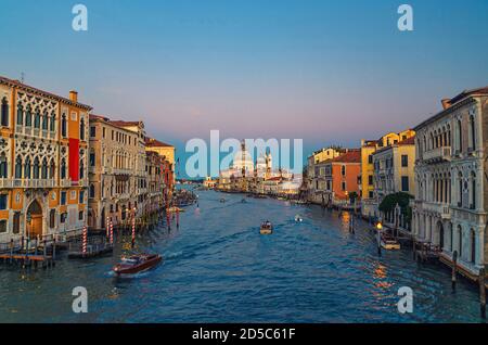 Paysage urbain de Venise avec voie navigable du Grand Canal. Bâtiments avec lumières le long du Grand Canal. Santa Maria della Salute Église catholique romaine sur Punta della Dogana au crépuscule. Vénétie, Italie. Banque D'Images