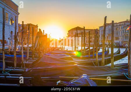 Gondoles amarrées sur l'embarcadère de la voie navigable du Grand Canal à Venise. Bâtiments de style baroque le long du canal Grande. Vue contre le soleil. Paysage urbain incroyable de Venise au coucher du soleil. Vénétie, Italie Banque D'Images