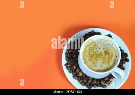 une tasse de café cappuccino avec de la crème chaude dans une tasse blanche sur fond orange avec des grains de café et une cuillère à café. vue du dessus. Banque D'Images