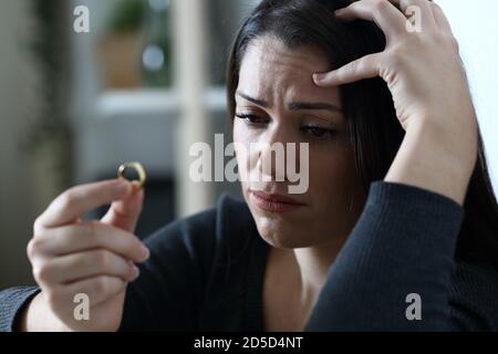 Triste femme douteuse regarde l'anneau de mariage de la pensée dans le divorce seul à la maison dans la nuit Banque D'Images