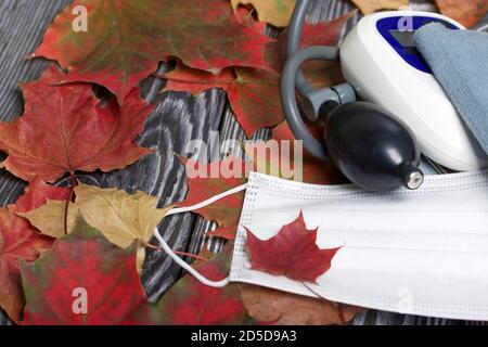 Tonomètre pour la mesure de la pression artérielle. Un masque médical se trouve à proximité. Parmi les feuilles d'érable d'automne. Banque D'Images