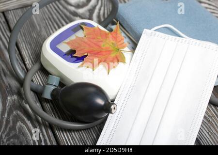 Tonomètre pour la mesure de la pression artérielle. Un masque médical se trouve à proximité. Parmi les feuilles d'érable d'automne. Banque D'Images