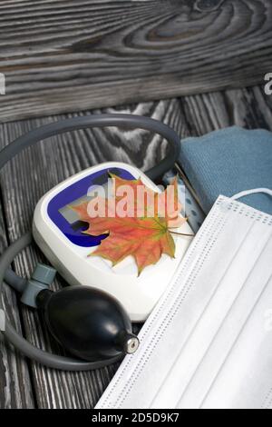 Tonomètre pour la mesure de la pression artérielle. Un masque médical se trouve à proximité. Parmi les feuilles d'érable d'automne. Banque D'Images