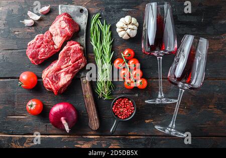 Viande de bœuf au-dessus de vieux cale de boucherie près des verres à vin rouge avec herbes et assaisonnements sur une ancienne table en bois sombre. Vue de dessus. Banque D'Images