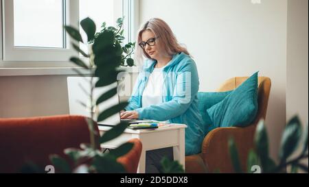 Une femme d'affaires caucasienne âgée occupée avec des lunettes utilise un ordinateur portable à la maison tout en travaillant à distance Banque D'Images