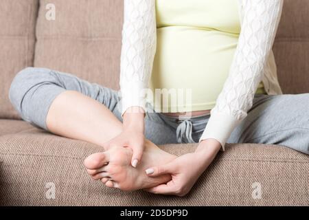 Crampes aux jambes pendant la grossesse. Gros plan des mains massant le pied gonflé tout en étant assis sur le canapé. Banque D'Images