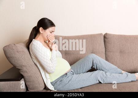 Grossesse matin maladie. Femme enceinte ayant des nausées se sentant mal dans le canapé à la maison. Banque D'Images