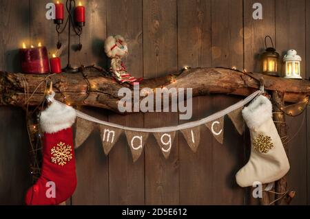 Sur une cheminée en bois faite de vieux rondins, il y a une bande de drapeaux avec l'inscription Magic, chaussettes blanc-rouge pour les cadeaux du Père Noël pendent sur le Banque D'Images