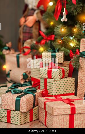 Une haute montagne de cadeaux sous un arbre de Noël dans des guirlandes de lumières en papier d'emballage d'artisanat rouge-vert avec boucles de ruban. Carte du nouvel an. Le Père Noël Banque D'Images