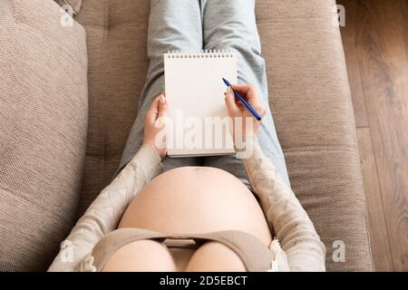 La femme enceinte prend des notes. Concept de grossesse, soins de santé, médecine. Mère attendant de bébé à la maison. Banque D'Images