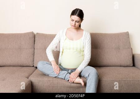 Crampes aux jambes pendant la grossesse. Gros plan des mains massant le pied gonflé tout en étant assis sur le canapé. Banque D'Images