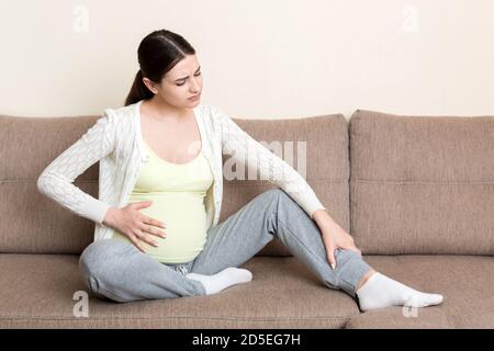 Crampes aux jambes pendant la grossesse. Gros plan des mains massant le pied gonflé tout en étant assis sur le canapé. Banque D'Images